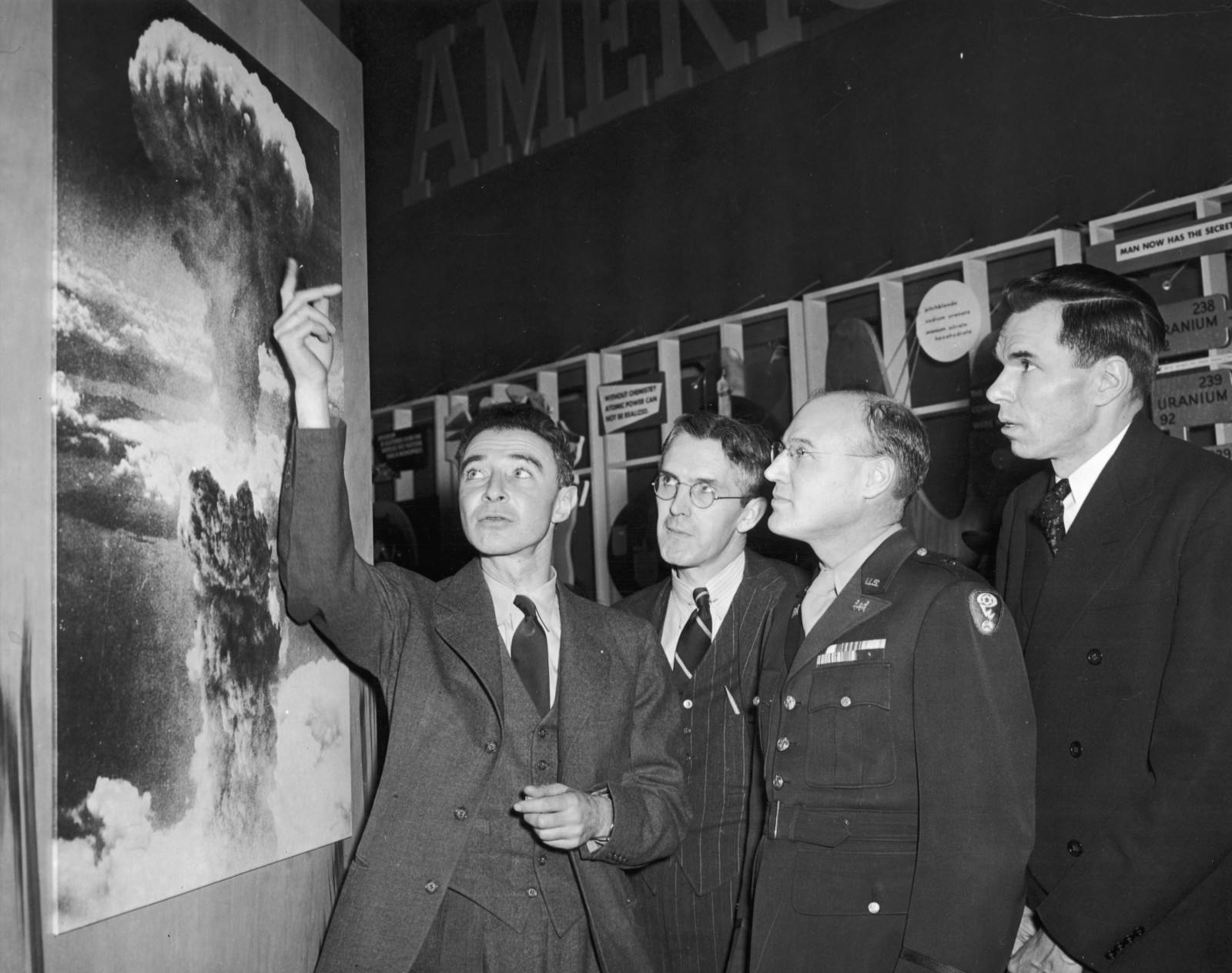 American physicist Dr. Robert Oppenheimer (1904 - 1967), points to a picture of the atomic bomb explosion over Nagasaki, Japan as scientist Henry D. Smyth (1898 - 1986) (second left), major General Kenneth D. Nichols (1907 - 2000) (second right), and scientist Glenn Seaborg (1912 - 1999) look on, 1940s (Hulton Archive/Getty Images)